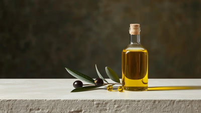 Minimalist still-life of a glass bottle of golden olive oil with a dropper, olives and an olive branch, styled in Oliiv's dark olive, green, lime and cream brand palette