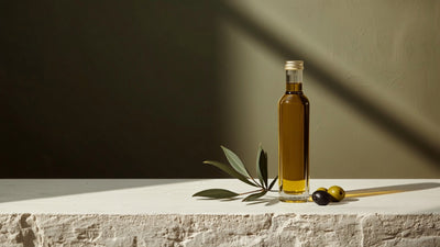 Minimalist still-life of a glass bottle of golden olive oil with olives and an olive branch, styled in Oliiv's dark olive, green, lime and cream brand palette